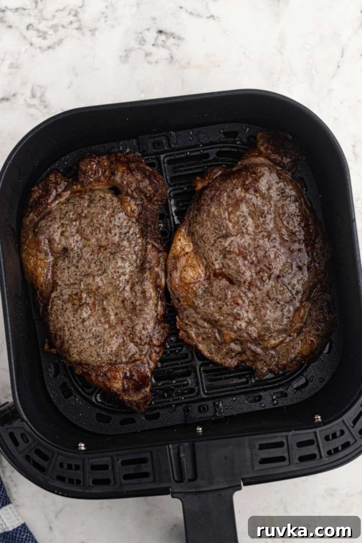 Ultimate Air Fryer Ribeye 5 Two juicy cooked ribeyes in the air fryer basket on a marble table.