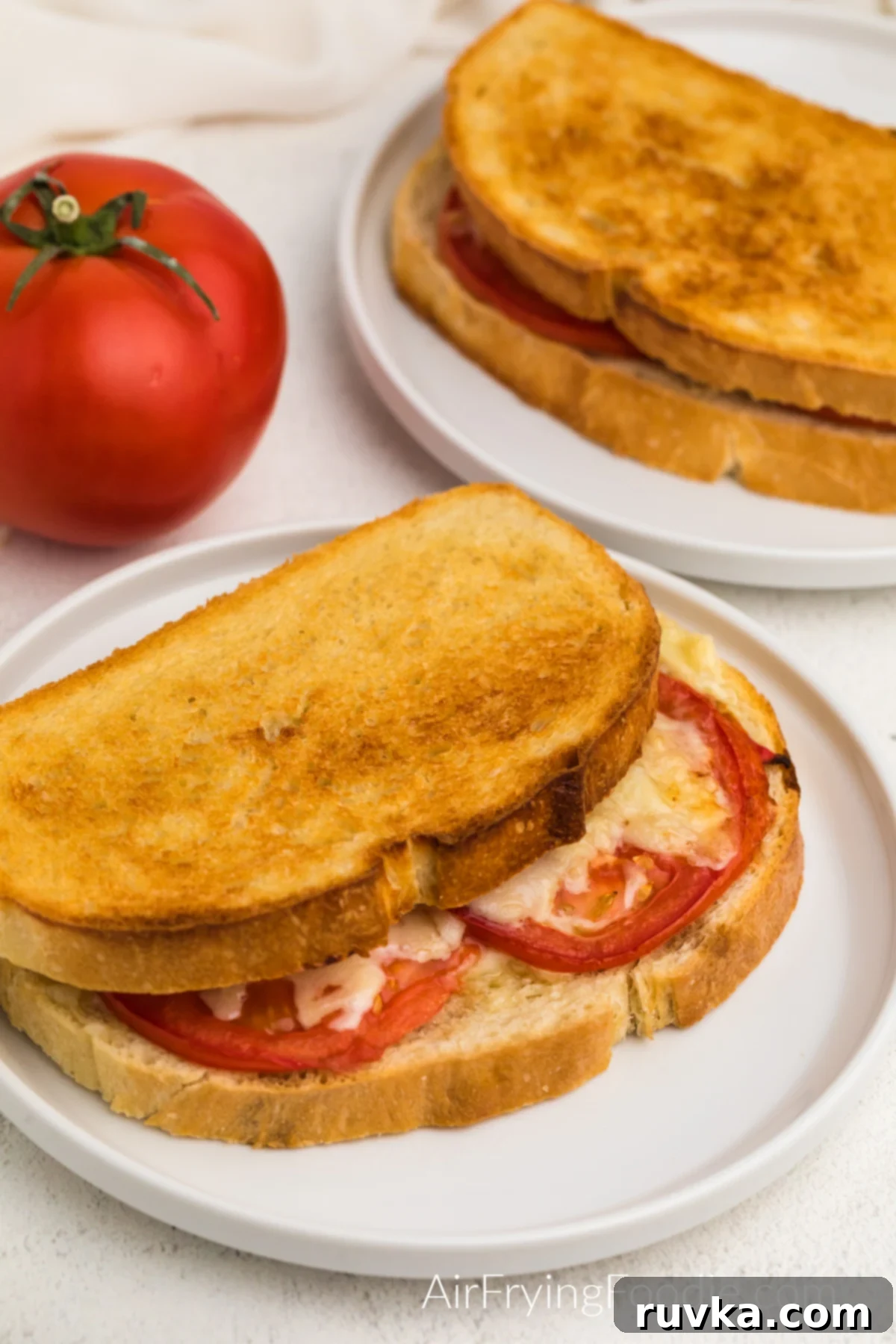 Crispy Air Fryer Tomato Cheese Melts 2 Tomato grilled cheese made in the air fryer and served on a white plate, showcasing its golden-brown exterior and melted cheese.