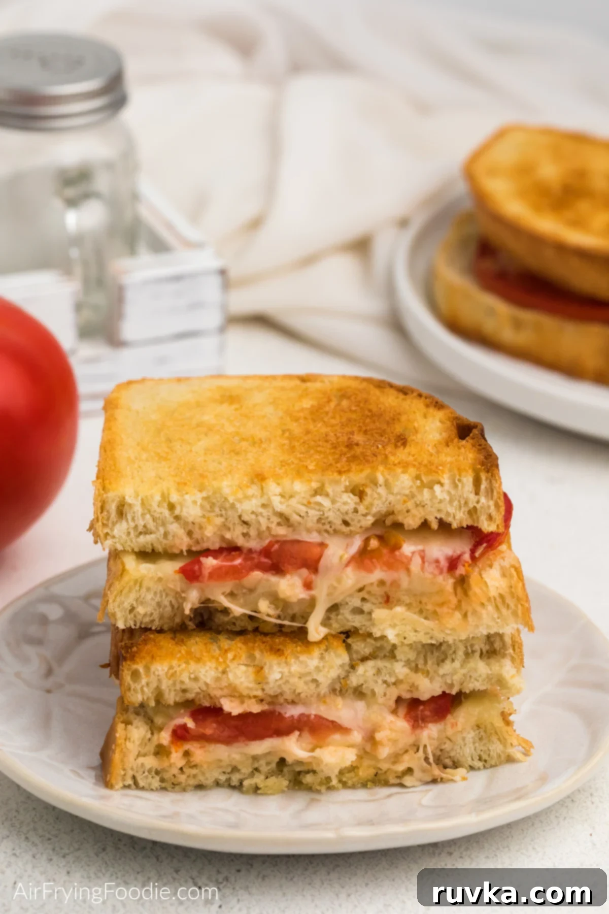 Crispy Air Fryer Tomato Cheese Melts 7 Sliced grilled tomato and cheese sandwich stacked in halves on a white plate, ready to be enjoyed.