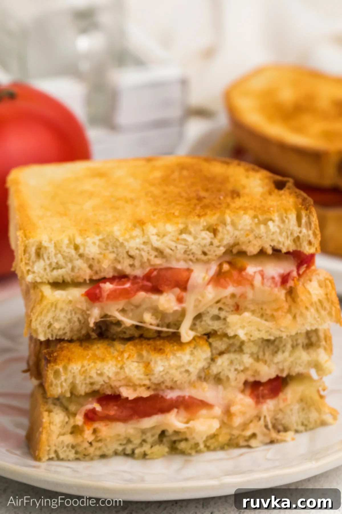 Crispy Air Fryer Tomato Cheese Melts 8 Golden brown grilled tomato and cheese sandwich sliced in half and stacked on a white plate, showcasing the crispy bread and melted cheese.