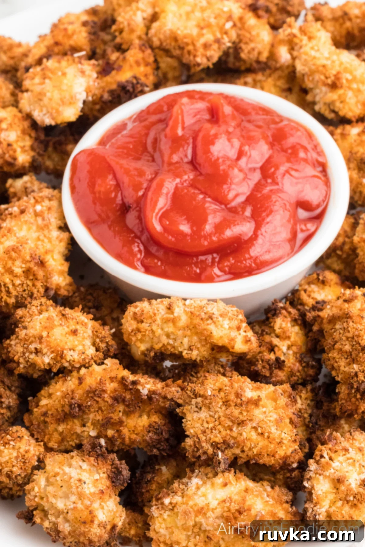 Air-Fried Chicken Poppers 2 Homemade popcorn chicken made in the air fryer, on a serving tray with a side of ketchup, showcasing its golden-brown crispiness.