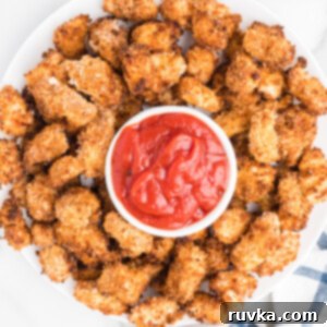 Air-Fried Chicken Poppers 10 A tray of crispy golden popcorn chicken on a serving plate with a bowl of ketchup for dipping.