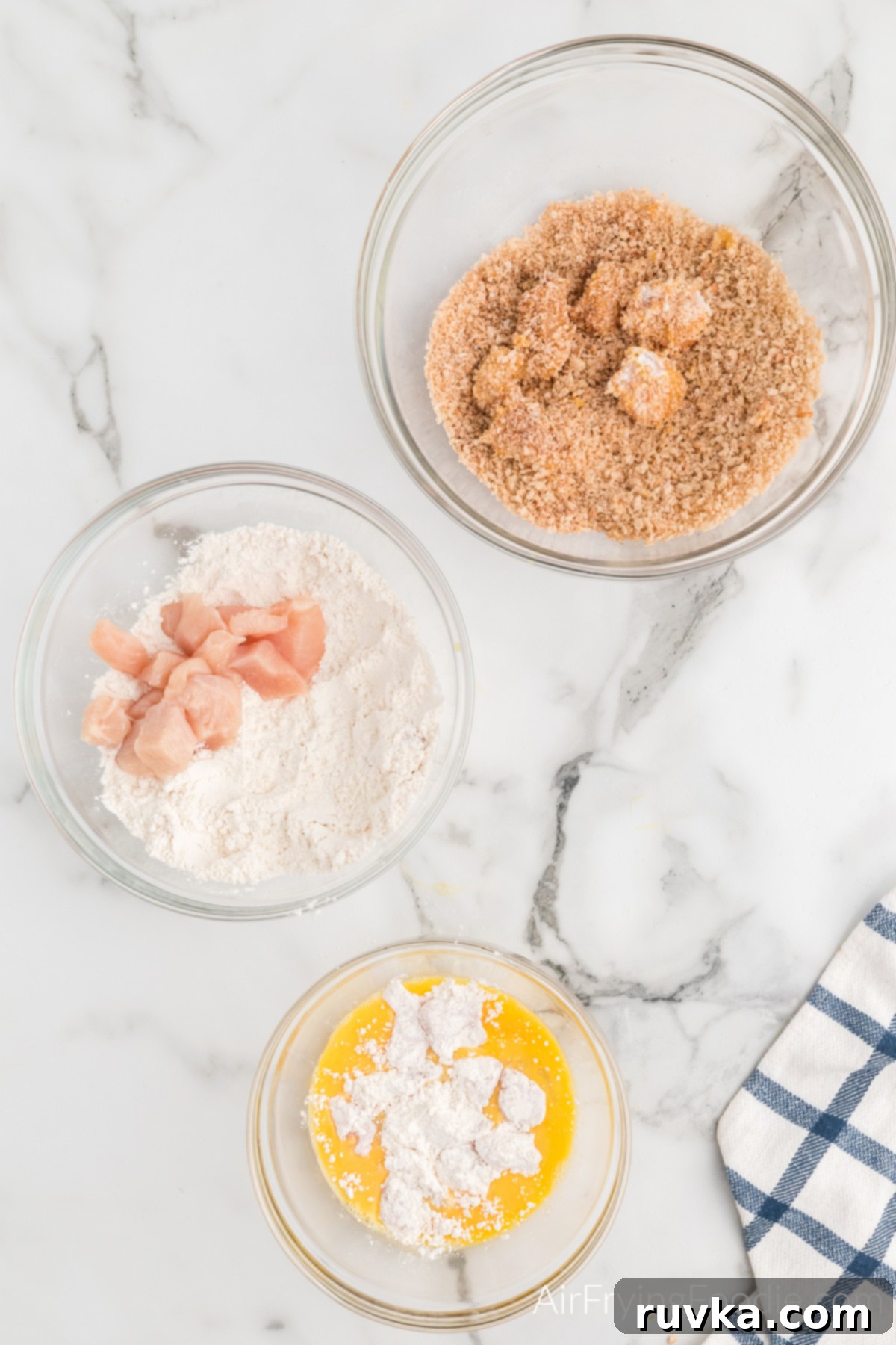 Air-Fried Chicken Poppers 5 Popcorn chicken undergoing the three-step dipping station process: flour, egg, and seasoned panko breadcrumbs for a perfect coating.