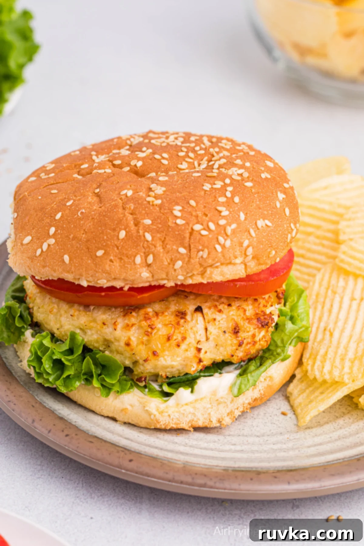 Crispy Air Fryer Chicken Burgers 2 Air Fryer Chicken burger on a bun with lettuce and tomato and a side of potato chips.