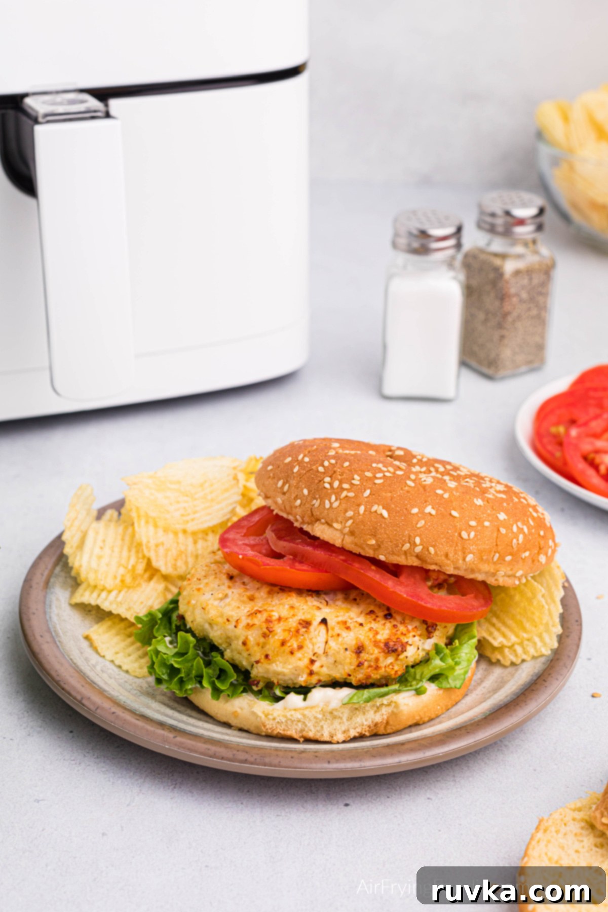 Crispy Air Fryer Chicken Burgers 9 Chicken burger dressed and ready to serve in a plate with potato chips with an air fryer in the background.