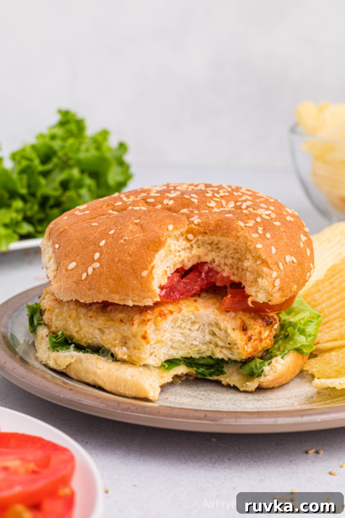 Crispy Air Fryer Chicken Burgers 10 Chicken burger on a plate with potato chips, with a bite missing.