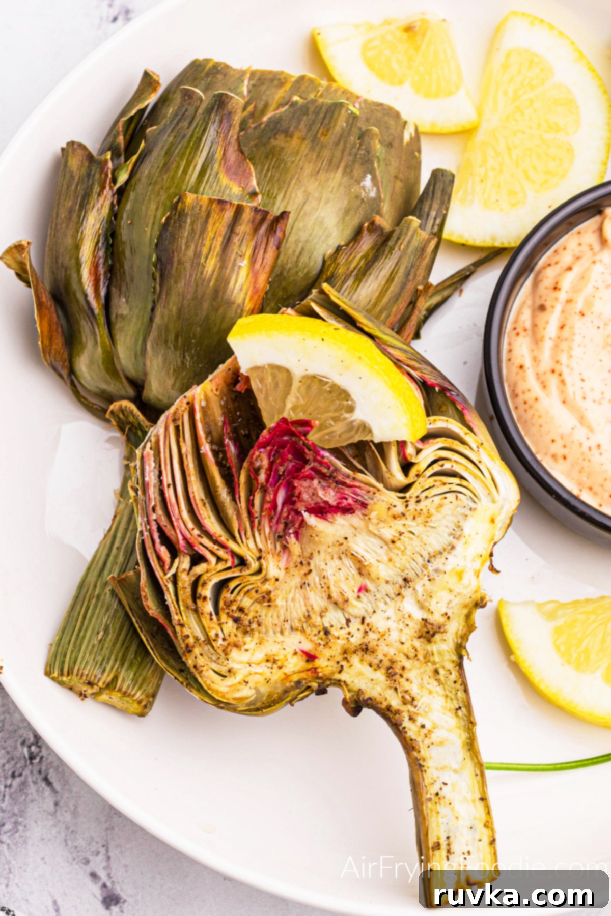 Air-Fried Artichoke Perfection 11 Close up of fried artichoke made in the air fryer and topped with a lemon slice, served with dipping sauce.
