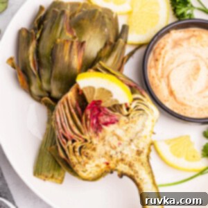 Air-Fried Artichoke Perfection 12 Air fryer artichoke on a white plate with a side of dipping sauce.