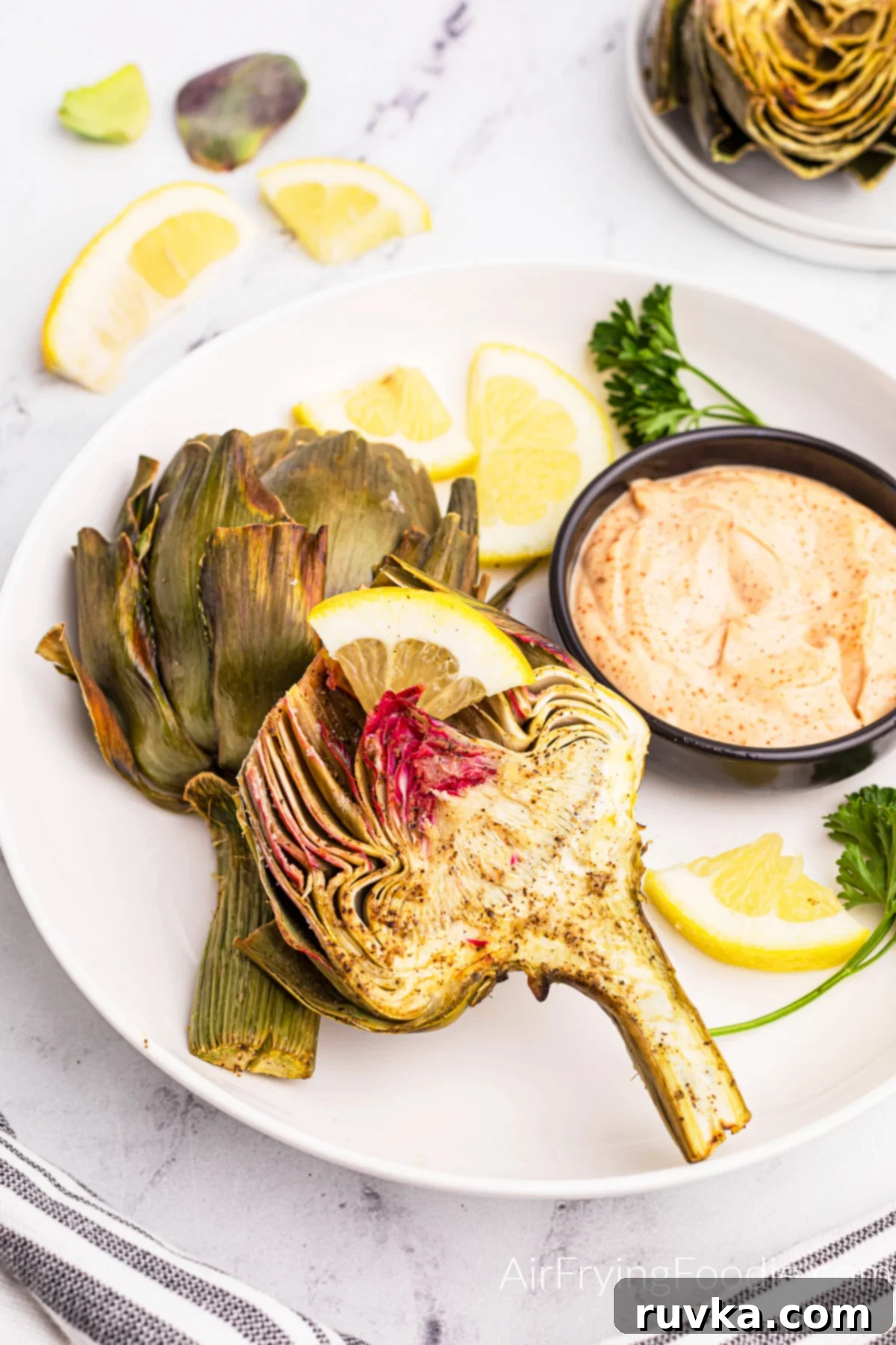 Air-Fried Artichoke Perfection 10 Air fried artichoke on a white plate with a side of lemons and dipping sauce.