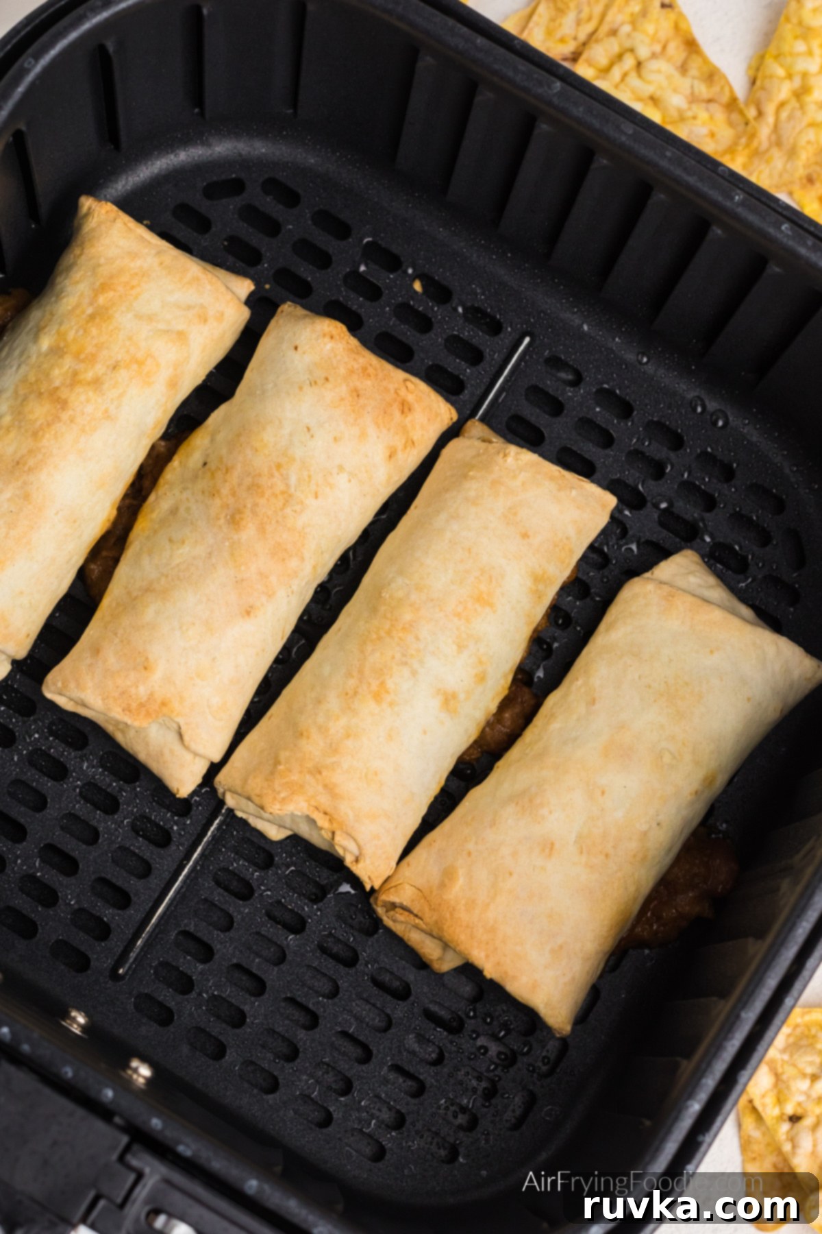 Perfectly Crispy Air Fried Frozen Burritos 6 Freshly air fried beef and bean burritos cooling slightly in the air fryer basket, steam gently rising, indicating they are hot and ready to be served.