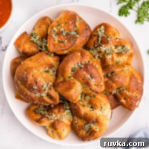 Quick Air Fryer Back to School Dinners 8 Golden bread knots with garlic and parmesan cheese stacked on a white plate with a small bowl of red sauce.