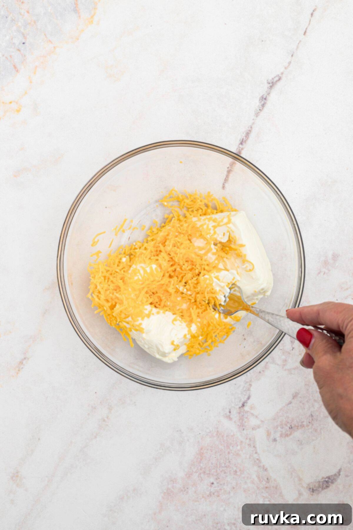 Crispy Air Fryer Jalapeño Poppers 5 In a medium clear glass bowl, shredded cheese and cream cheese are being mixed together with a fork.