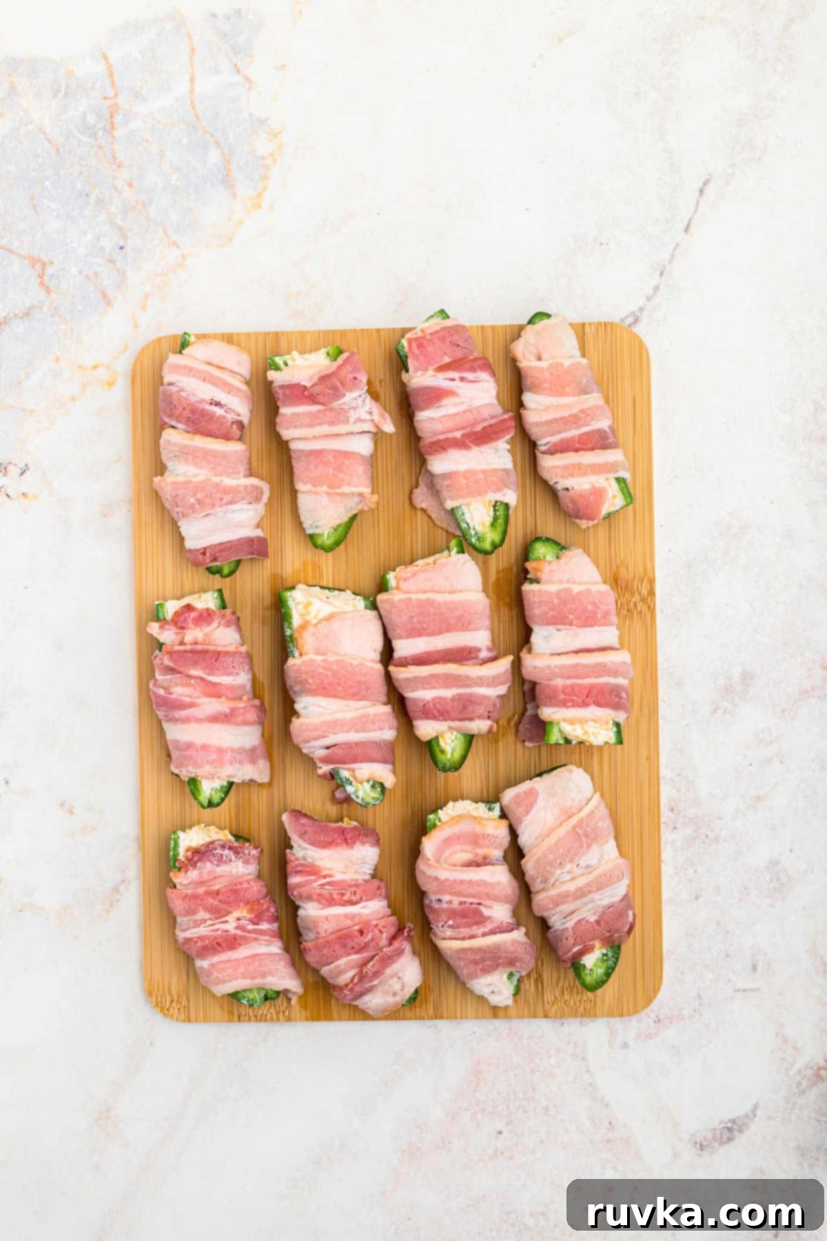 Crispy Air Fryer Jalapeño Poppers 7 Cheese stuffed jalapenos, wrapped in slices of bacon, on a wooden cutting board.