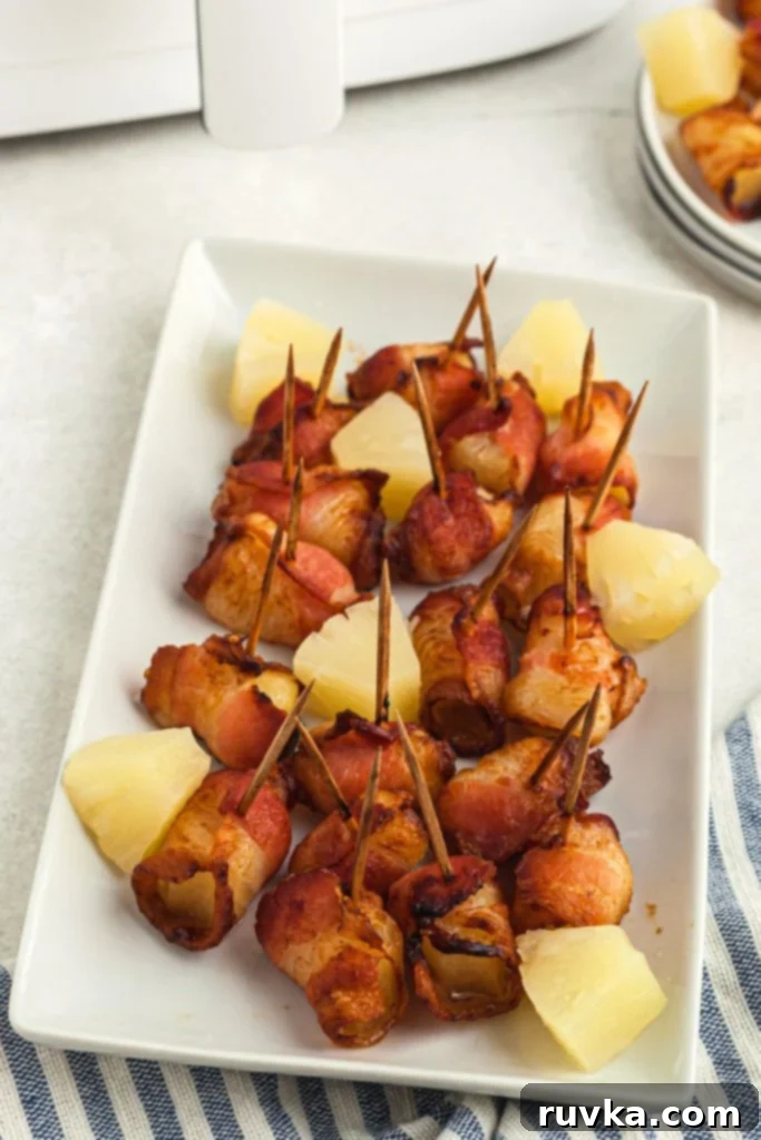 Air Fryer Bacon Pineapple Poppers 2 Crispy bacon wrapped pineapple bites on a long white plate in front of the air fryer, showcasing their golden perfection.