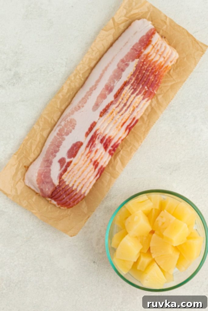 Air Fryer Bacon Pineapple Poppers 3 Bacon slices and pineapple chunks ready for preparation on a white marble table.