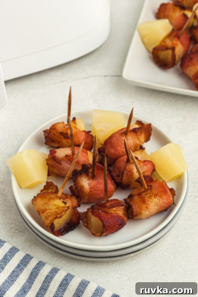 Air Fryer Bacon Pineapple Poppers 7 Crispy bacon wrapped pineapple chunks served on a small elegant white plate, ready to be enjoyed.