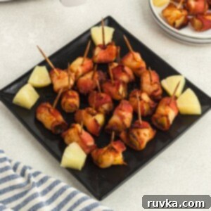Air Fryer Bacon Pineapple Poppers 8 Crispy bacon wrapped pineapple bites on a square black plate, perfectly cooked.