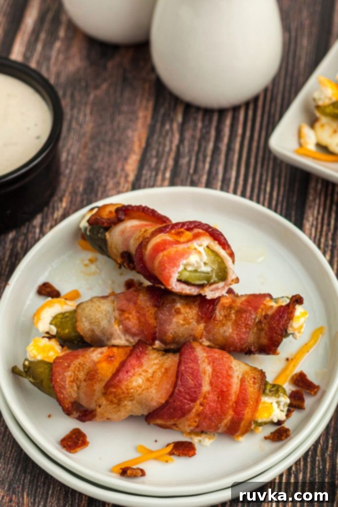 Air-Fried Pickle Bites 8 Stuffed pickle with cream cheese and wrapped in bacon on a small white plate.