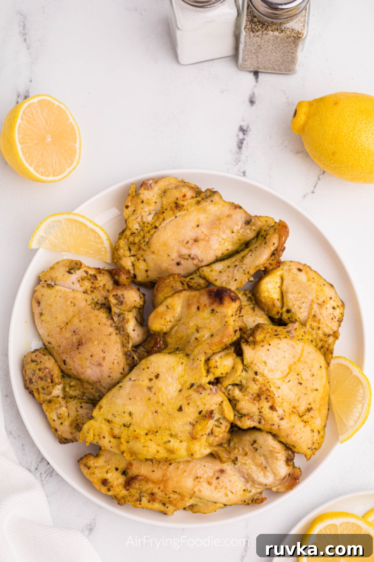 Crispy Air Fryer Lemon Pepper Chicken Thighs 2 Crispy Air Fryer Lemon Pepper Chicken Thighs served on a white plate with fresh lemon wedges and parsley garnish.