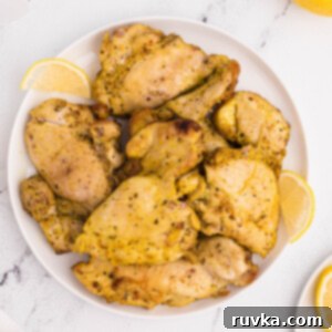 Crispy Air Fryer Lemon Pepper Chicken Thighs 10 Air fried Lemon pepper chicken thighs on a white plate with lemon slices.