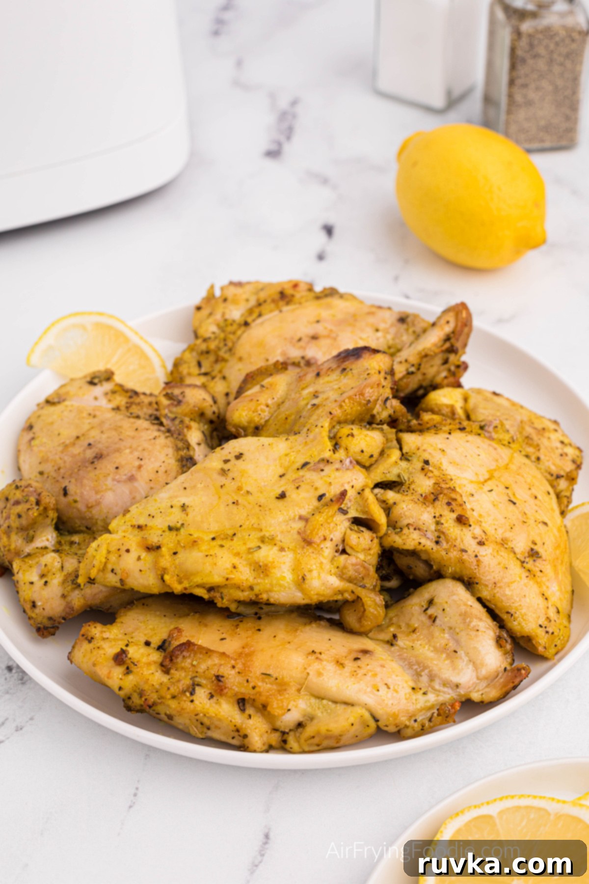 Crispy Air Fryer Lemon Pepper Chicken Thighs 8 A serving of crispy Air Fryer Lemon Pepper Chicken Thighs on a white plate, garnished with fresh lemon wedges.