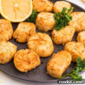 Crispy Air Fryer Scallops 9 Golden juicy scallops on a dark plate seasoned and served with lemon wedges.