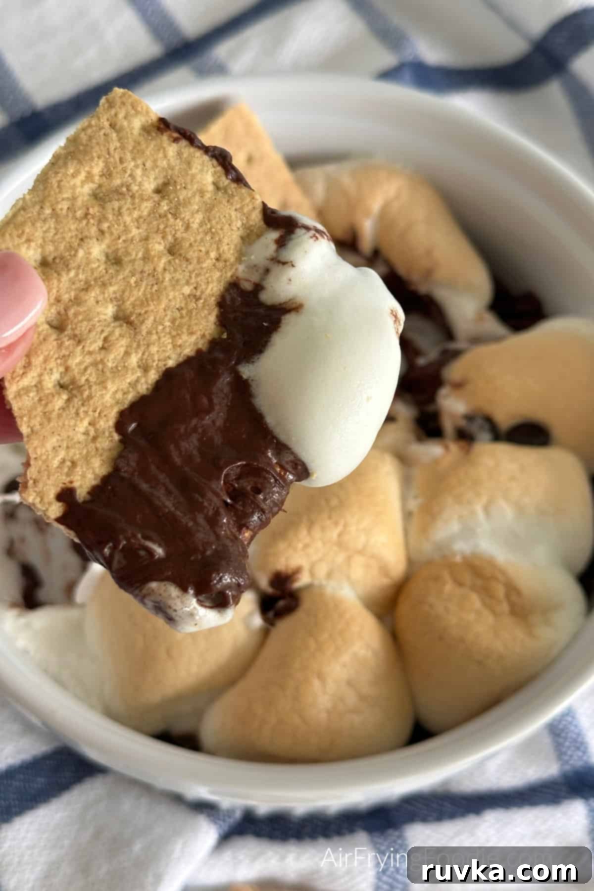 Air Fryer S'mores Dip 2 Graham cracker being dipped into S'more Dip that was made in a glass dish in the air fryer.