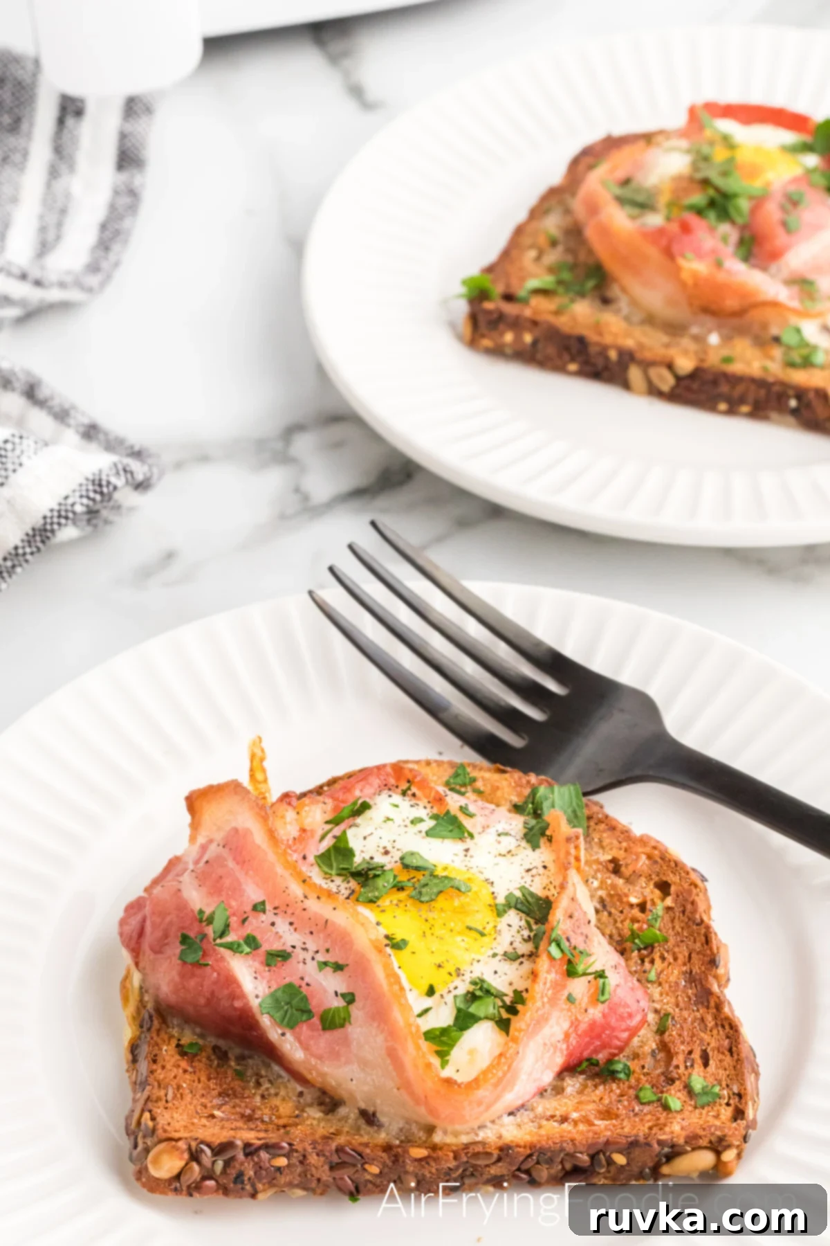 Easy Air Fryer Breakfast Sandwich 2 Fully cooked air-fried egg and bacon on a piece of wheat toast sprinkled with parsley served on a white plate with a fork.