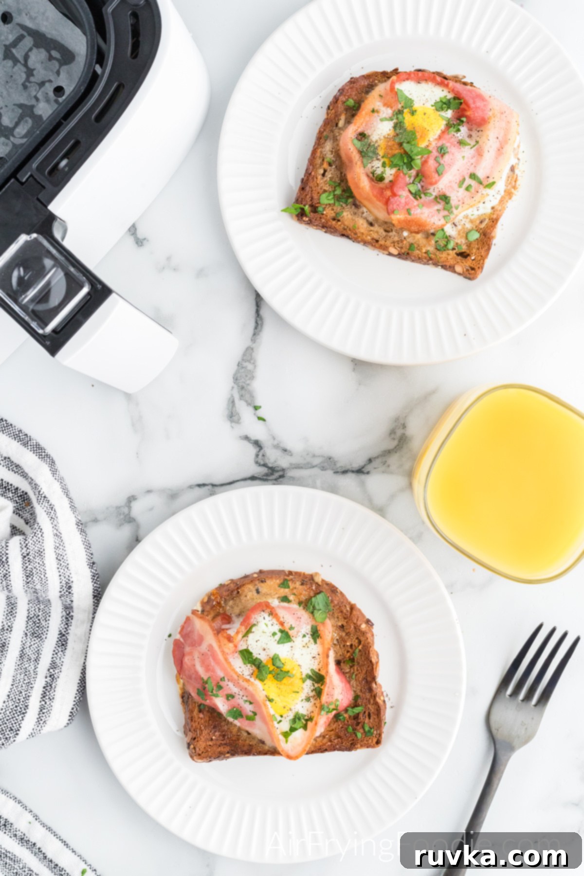 Easy Air Fryer Breakfast Sandwich 8 Overhead shot of fully cooked toast with bacon and eggs on two round plates sprinkled with parsley served with a glass of orange juice with a fork.