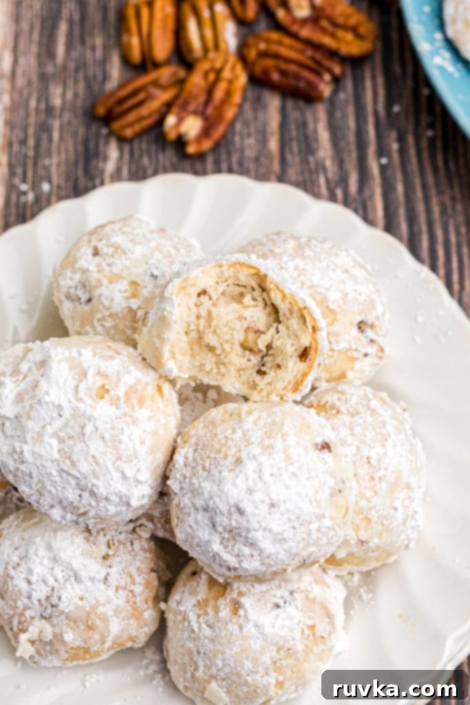 Easy Air Fryer Snowball Cookies 11 Golden air fried cookies rolled in powdered sugar and stacked on a white plate with one small bite taken