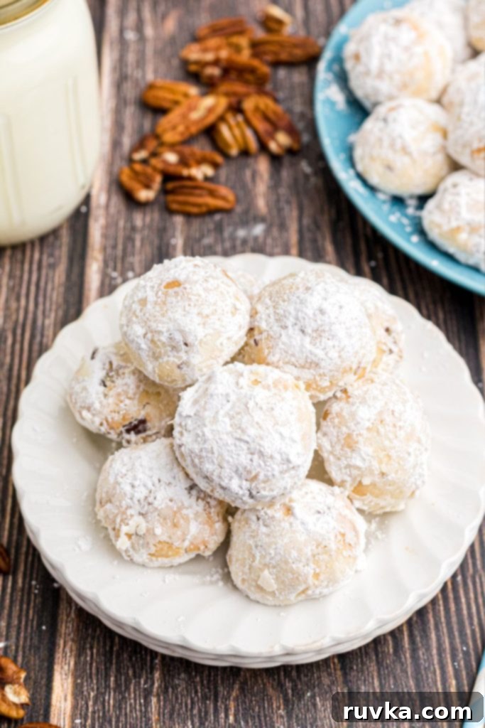 Easy Air Fryer Snowball Cookies 12 White plate with stacked powdered sugar coated snowball cookies on a wooden table
