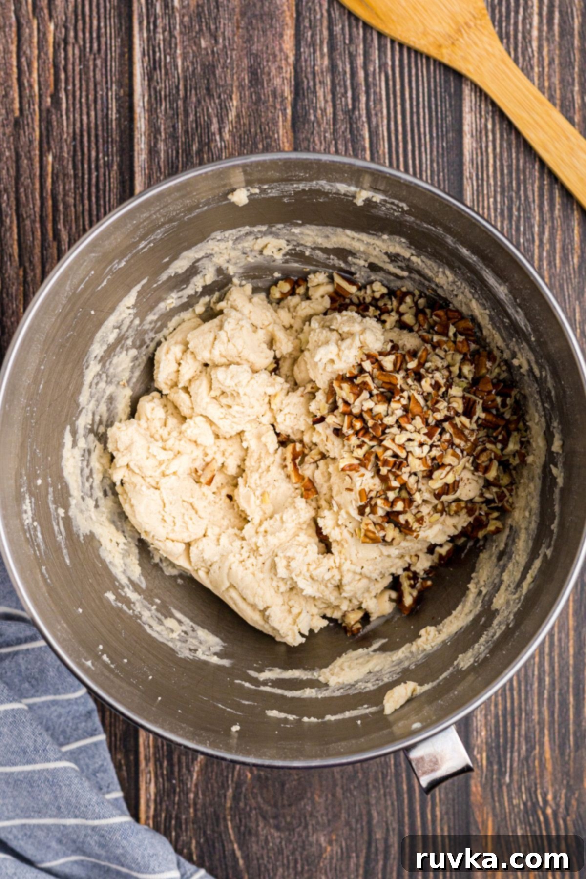 Chopped pecans being folded into cookie dough with a rubber spatula
