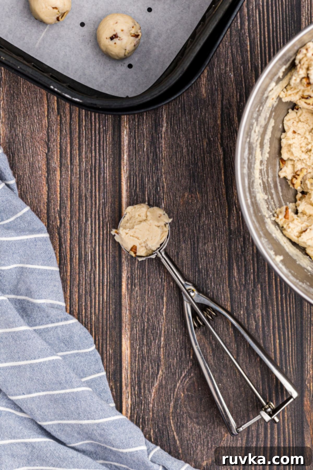 Scoop of dough on a wooden table while balls of dough are in air fryer basket