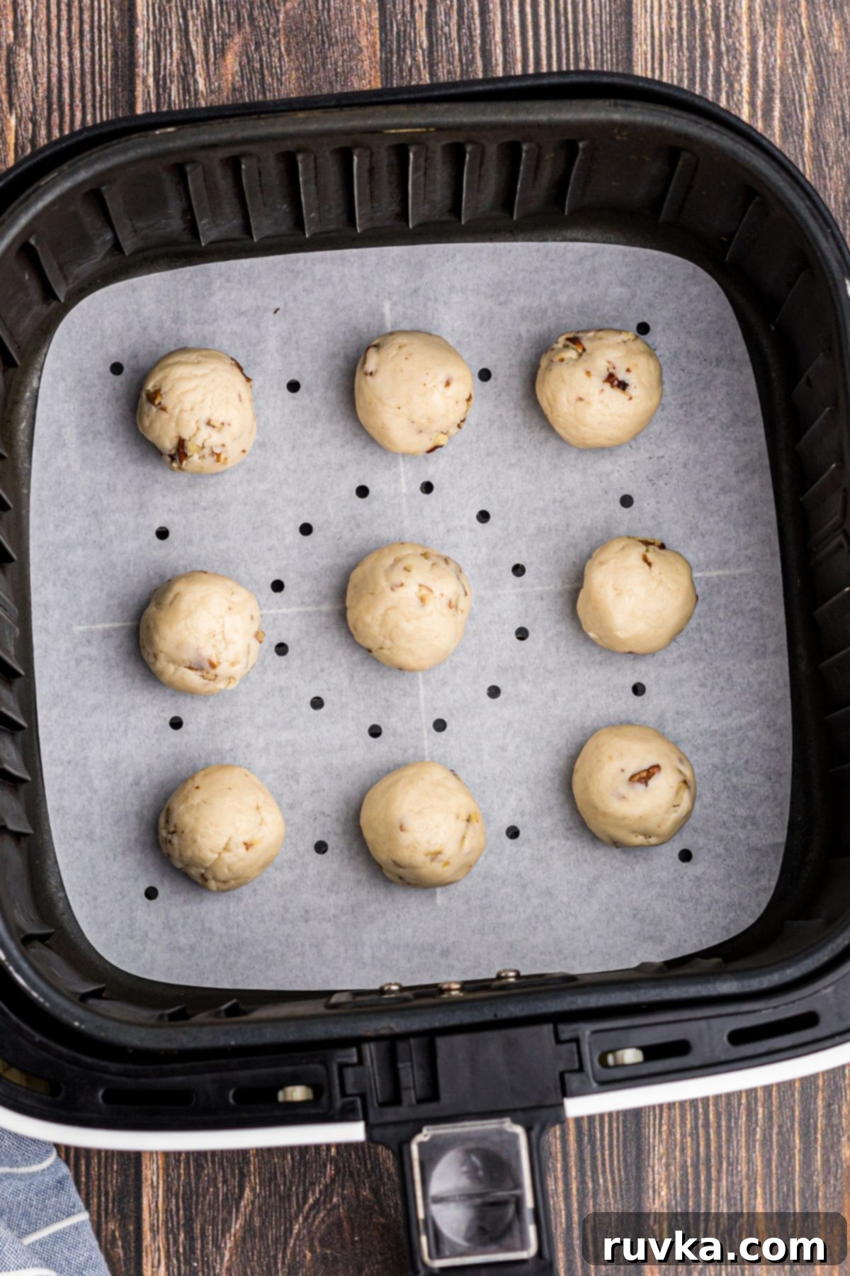 Cookie dough balls arranged in an air fryer basket lined with parchment paper