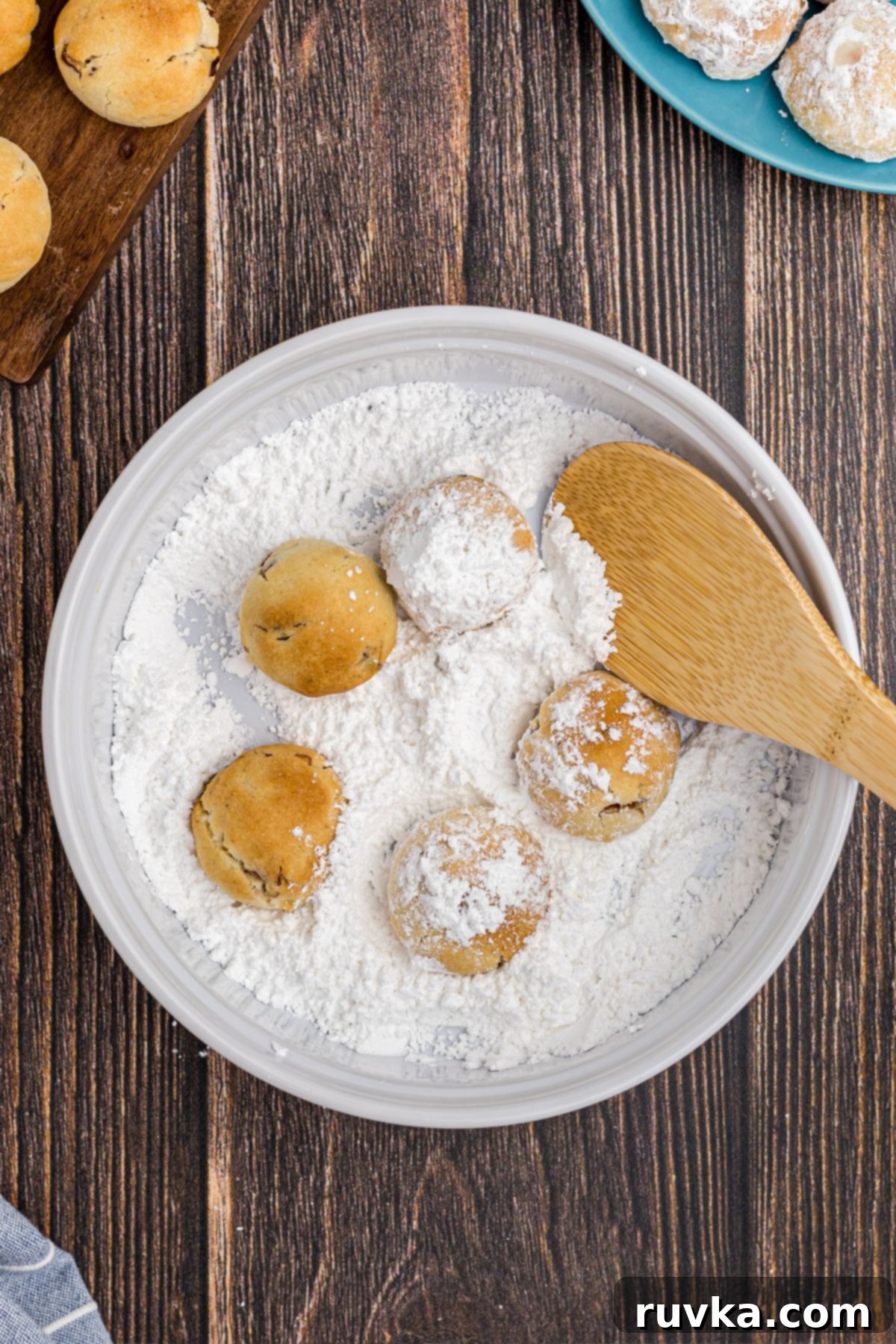Snowball cookies being coated in powdered sugar in a bowl