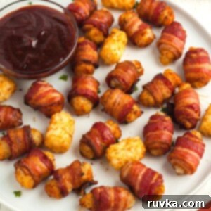 Crispy Air Fryer Bacon-Wrapped Tater Tots 11 Golden and crispy bacon wrapped tater tots on a white round plate served with bbq sauce