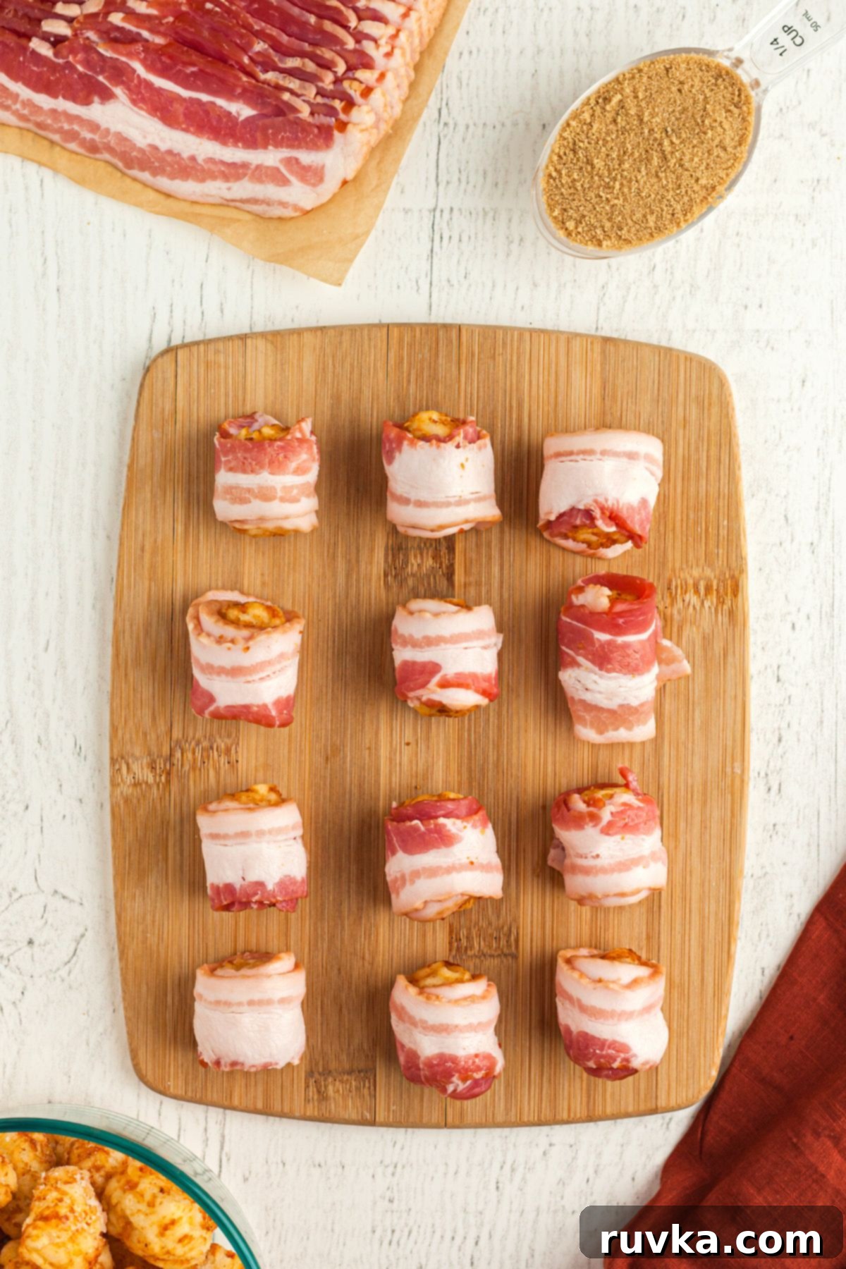 Crispy Air Fryer Bacon-Wrapped Tater Tots 5 Tater tots wrapped in slices of bacon on a wooden cutting board