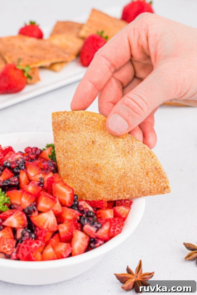 Crispy Air Fryer Cinnamon Sugar Tortilla Chips 10 A hand lifting a cinnamon sugar tortilla chip out of a bowl of chopped fruit