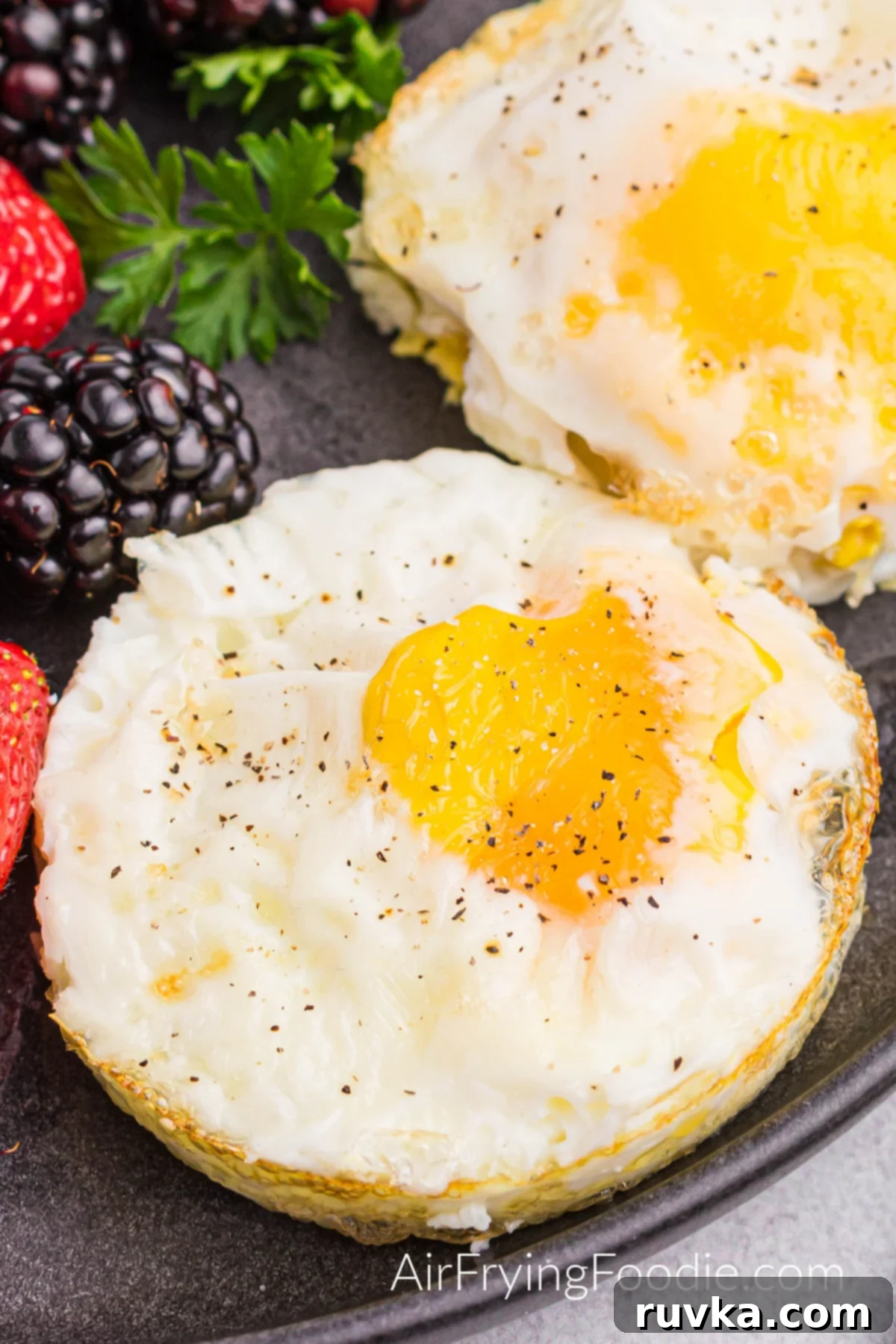 Perfect Air Fried Eggs 2 Fried eggs on a plate topped with salt and pepper and a side of fresh fruit, showcasing a perfect sunny side up yolk.