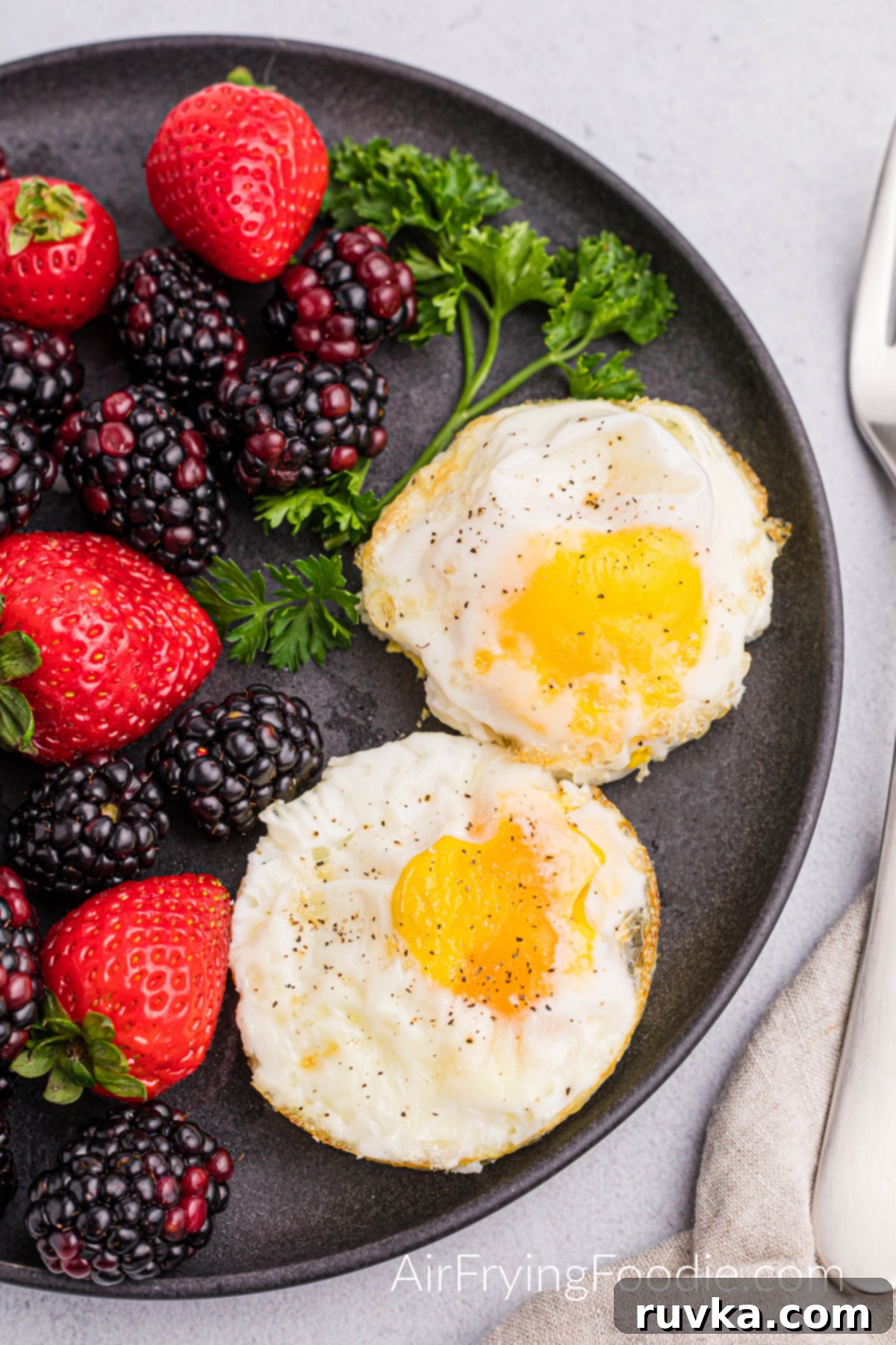 Perfect Air Fried Eggs 6 Two perfectly air-fried sunny-side-up eggs, seasoned with salt and pepper, served on a plate with a side of mixed berries and orange slices.