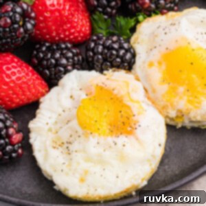 Perfect Air Fried Eggs 8 Air fryer fried eggs topped with salt and pepper and served on a dark plate with a side of fruit.