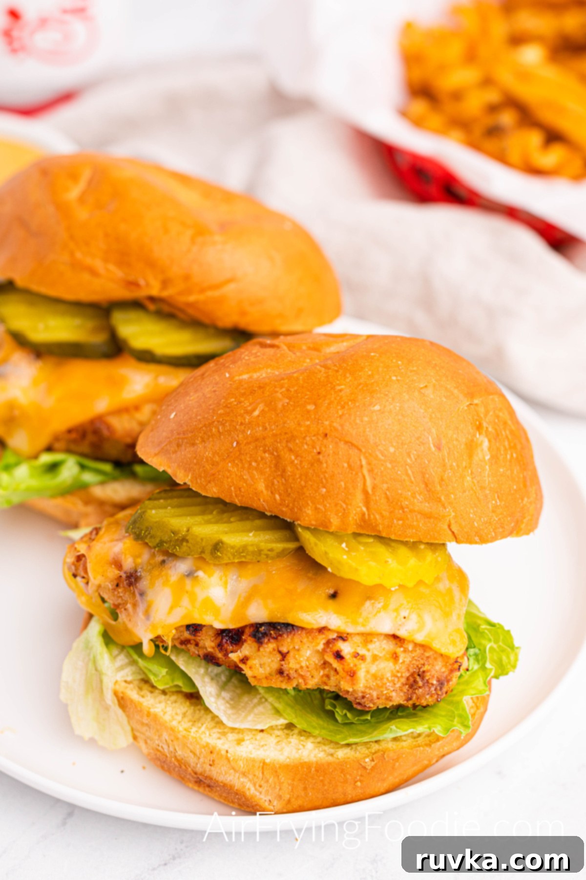 Crispy Homemade Air Fryer Chick-fil-A 13 Chick fil a copycat sandwich fully cooked and dressed with pickles, cheese, lettuce, and sauce in a red basket. A small portion of a red basket with waffle fries is in the top right of the picture.