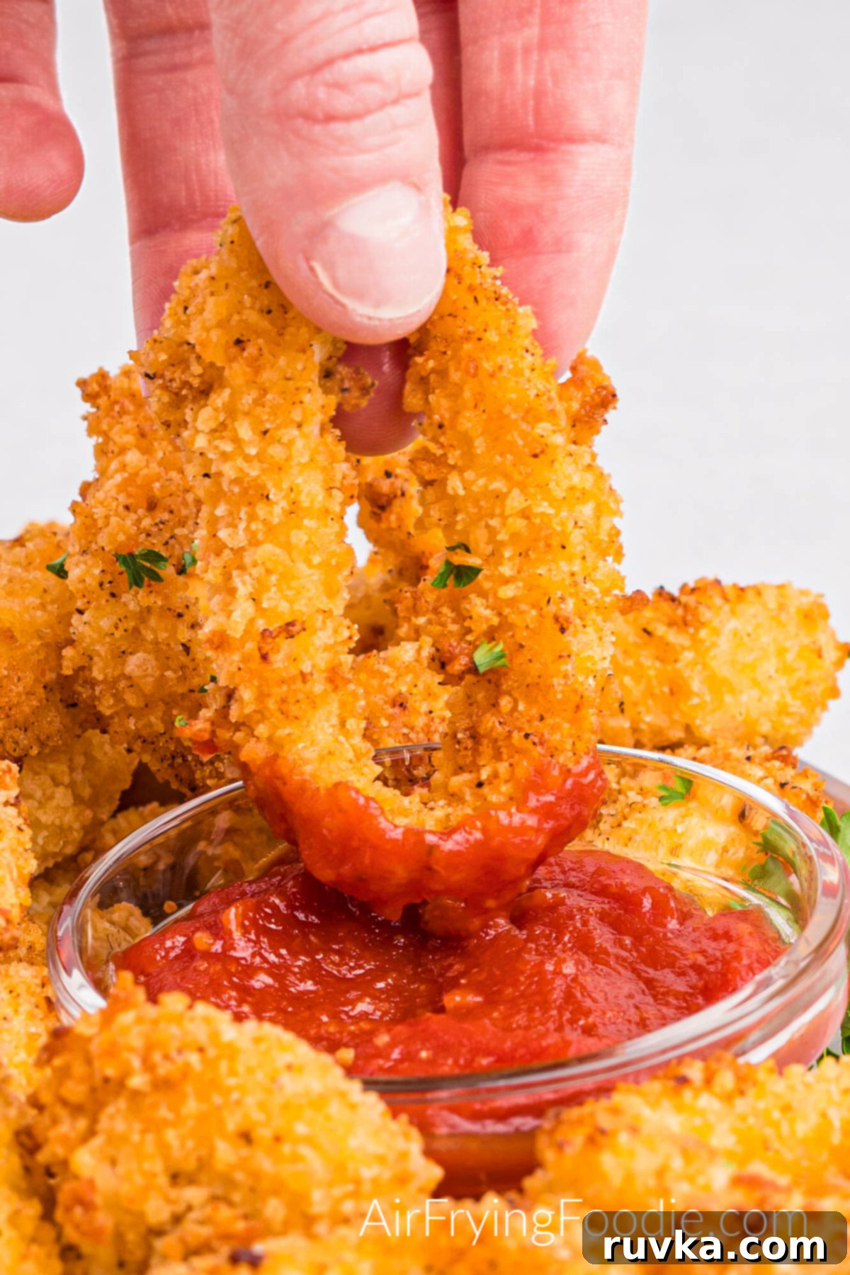 Crispy Air Fried Calamari 12 A close-up picture of golden brown calamari cooked in the air fryer with one piece of calamari dipped in a small glass bowl with cocktail sauce.
