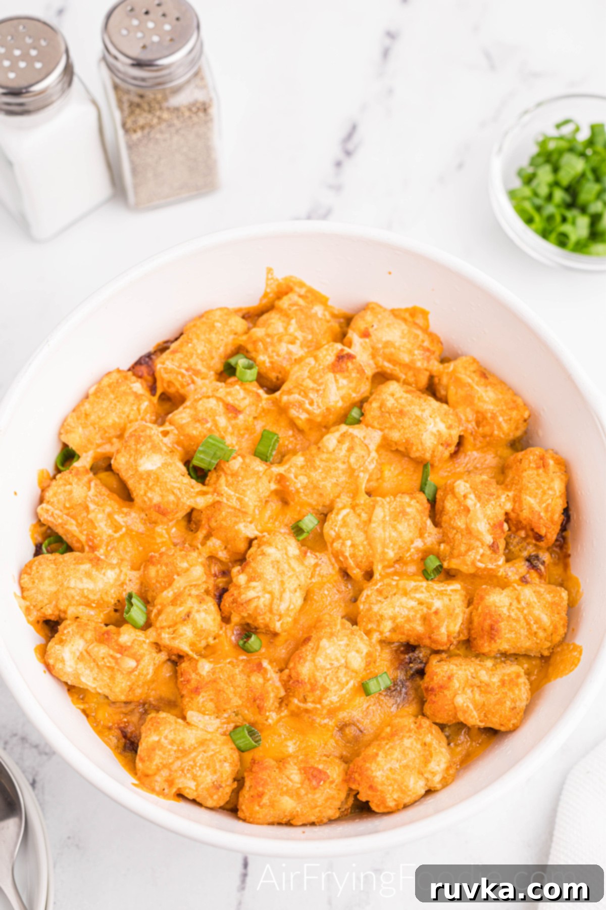 Hearty Air Fryer Cowboy Casserole 11 Overhead shot of a fully cooked and ready-to-serve cowboy casserole made in the air fryer with a small clear bowl of chives and salt and pepper shakers.