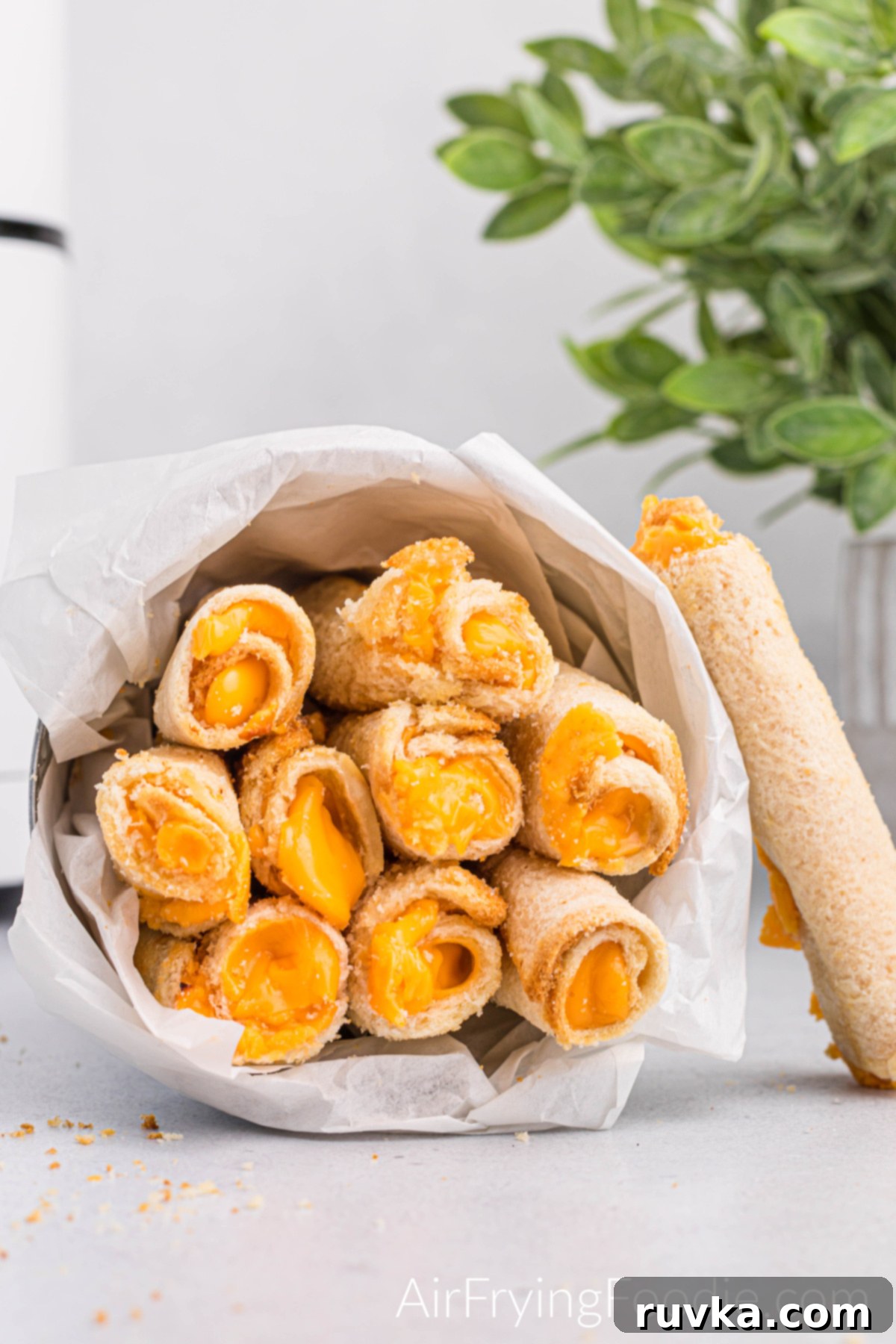 Crispy Cheesy Air Fryer Roll Ups 2 Fully cooked grilled cheese roll ups in a tin container laying on its side with one roll up leaning against the tin container.