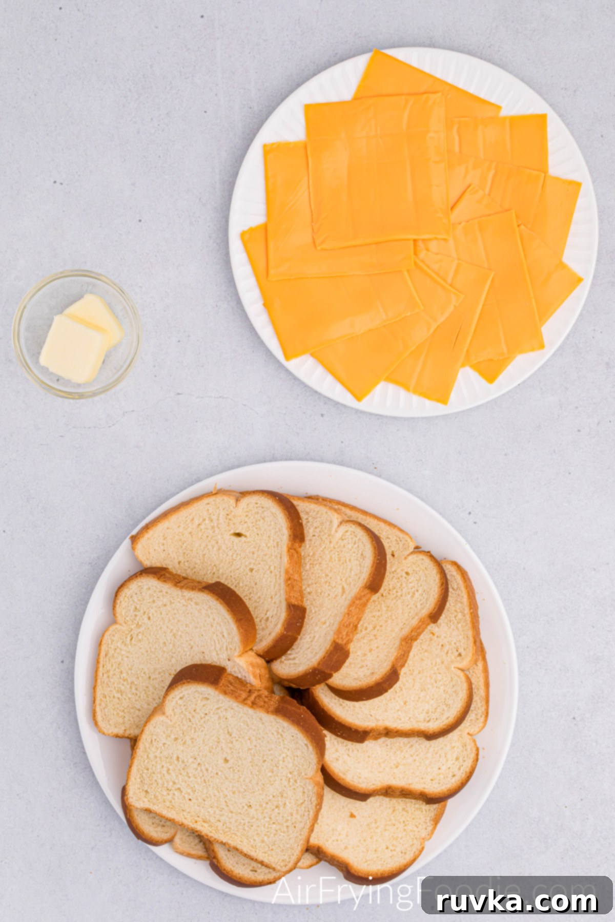 Crispy Cheesy Air Fryer Roll Ups 3 Bread overlapping in a circle on a round white plate. American cheese covering the bottom of a round white plate and a ramekin on butter.