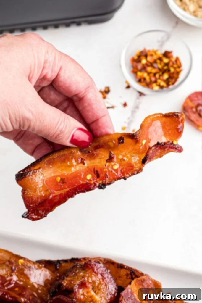 Crispy Sweet Air Fryer Bacon 8 Juicy spicy bacon slices being held by a hand over the large plate.