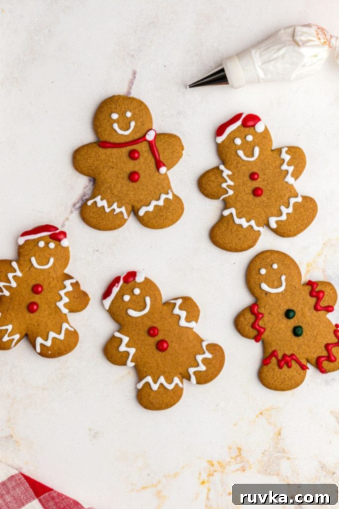 Quick and Easy Air Fryer Gingerbread Delights 11 Golden gingerbread men cookies arranged on a marble table, being carefully frosted with white icing, ready for holiday decoration.