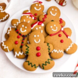 Quick and Easy Air Fryer Gingerbread Delights 13 Golden gingerbread cookies on a white plate frosted with red, white, and green frosting, showcasing festive decoration.