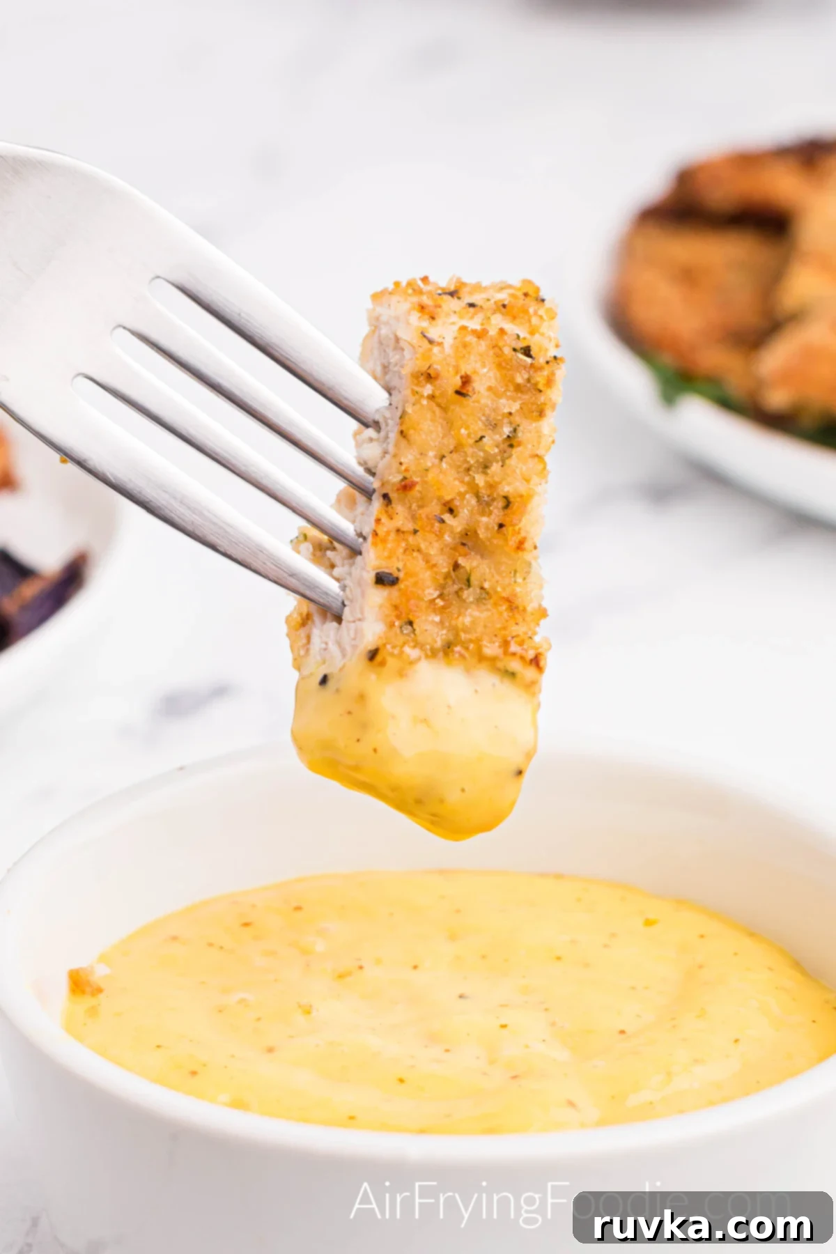 Perfectly Golden Air Fryer Chicken Cutlets 8 A white bowl of creamy honey mustard sauce with a piece of fully cooked chicken from the air fryer on a fork dipped in the creamy honey mustard sauce.
